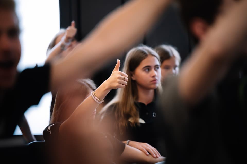 Ein Klassenzimmer, in dem sich viele Schüler melden und den Daumen hoch zeigen.
